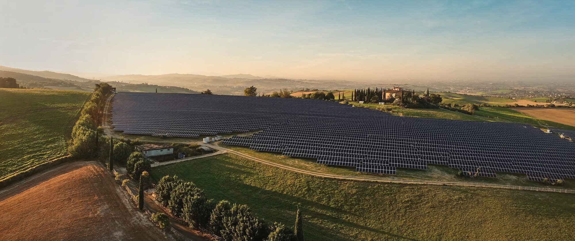 Impianto fotovoltaico a terra al tramonto, con campagna coltivata sullo sfondo